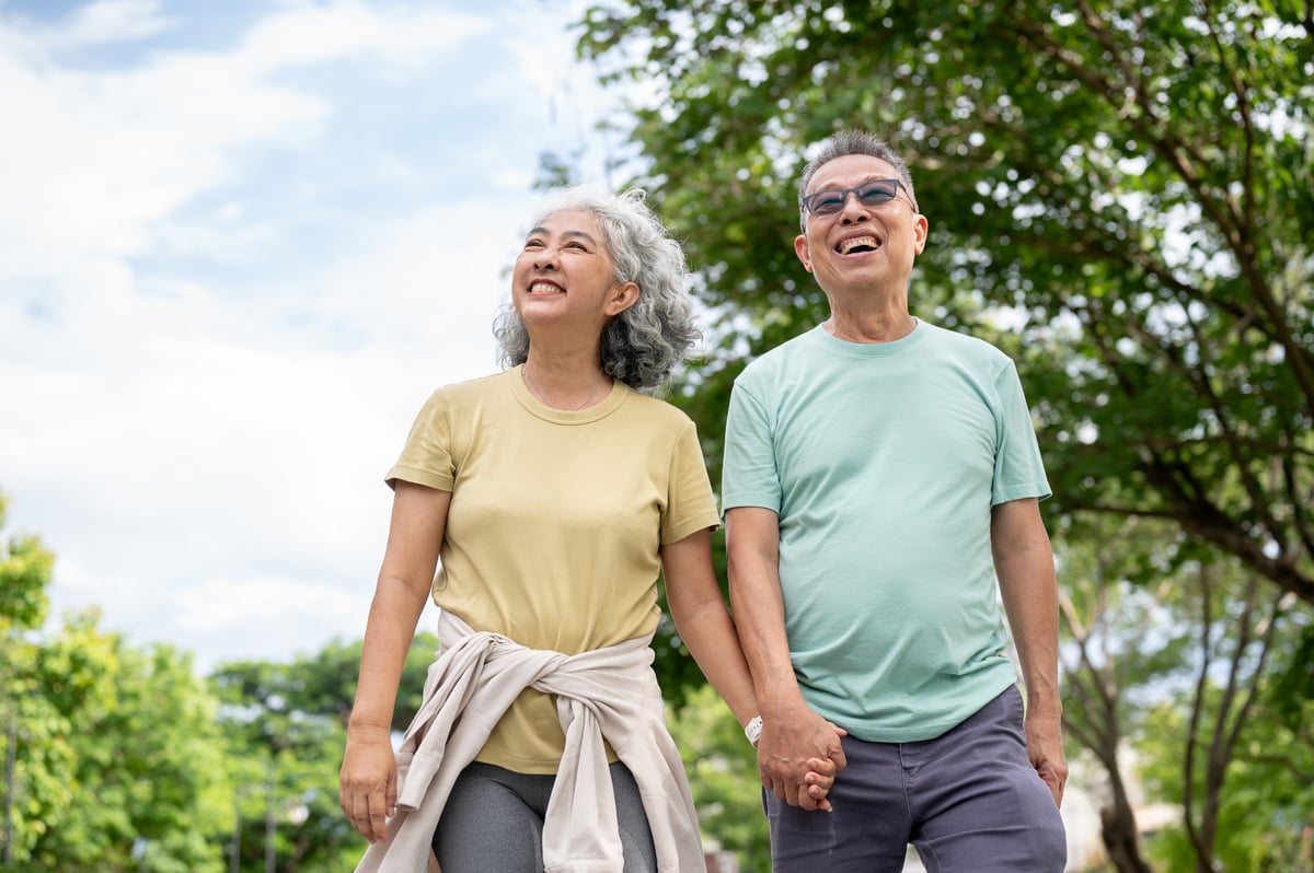 Glasses old man smiling and holding hand with old woman while walking together after exercise in park. Elderly couple, Green Nature, Chilling Outdoor.
