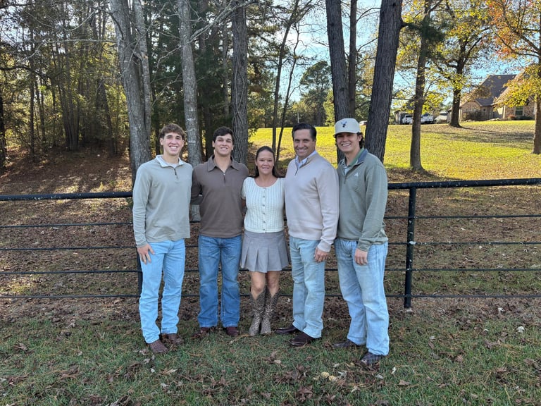 Five people standing together at a farm gate with trees and open fields in the background
