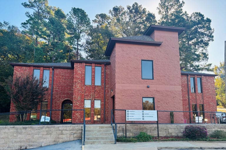 Modern red brick building with geometric architecture and large windows, surrounded by trees on a clear day